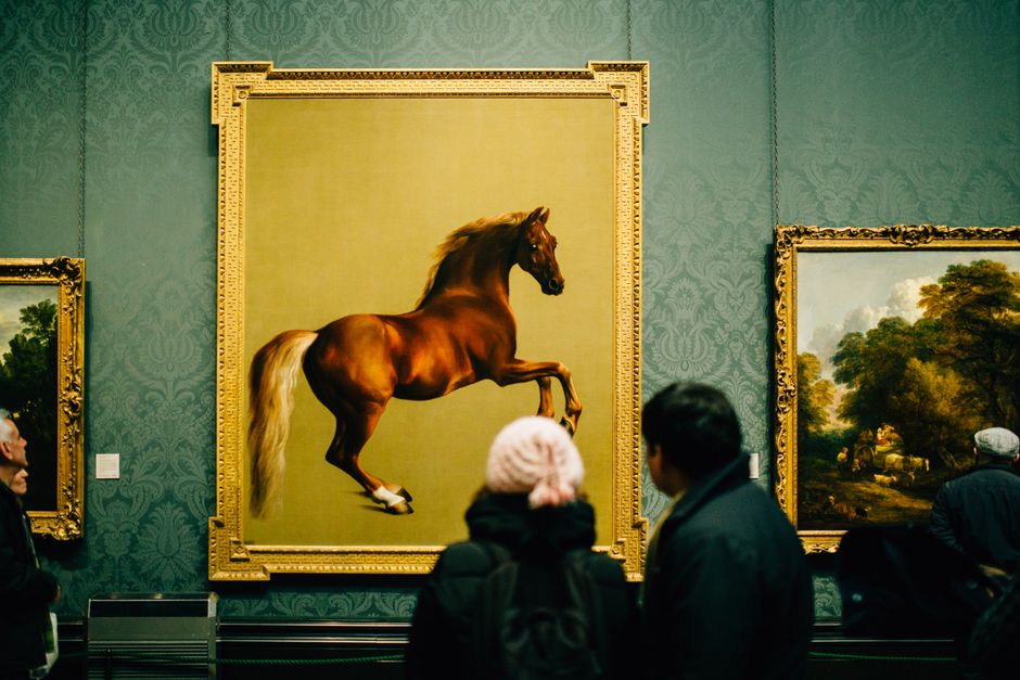 Paardenschilderij boven knusse bank met kussens.